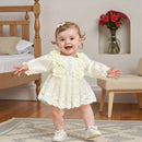 Bebê sorridente vestindo vestido branco com flores e sapatinhos em quarto acolhedor